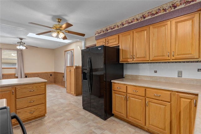 kitchen featuring a wainscoted wall, wood walls, light countertops, ceiling fan, and black refrigerator with ice dispenser