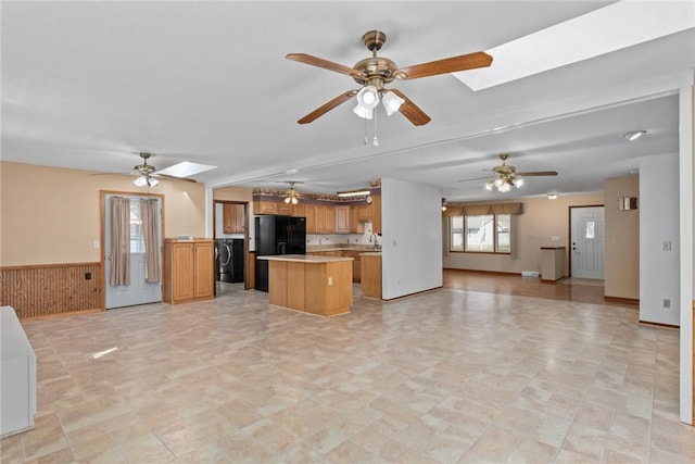 kitchen featuring a ceiling fan, open floor plan, freestanding refrigerator, a skylight, and washer / dryer