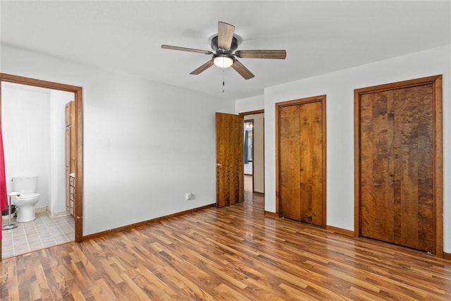 unfurnished bedroom with wood finished floors, baseboards, and two closets