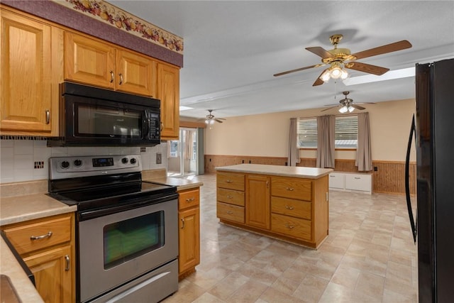 kitchen featuring a wainscoted wall, black appliances, wooden walls, light countertops, and ceiling fan