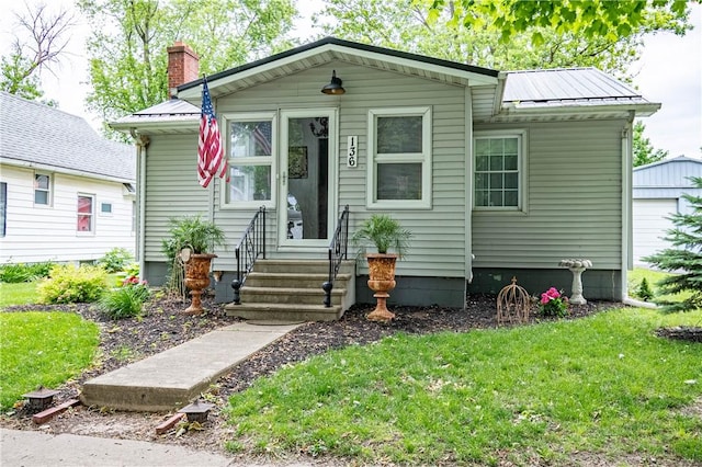 136 S High St, Lovington, IL 61937 - bungalow-style home featuring a chimney, metal roof, a front yard, and a garage