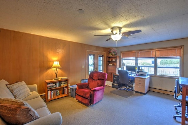 carpeted office space featuring a baseboard heating unit, ceiling fan, and wooden walls