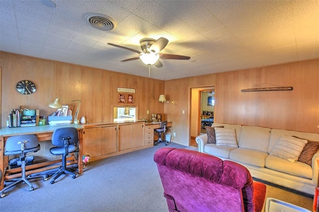 carpeted living room with ceiling fan and wooden walls