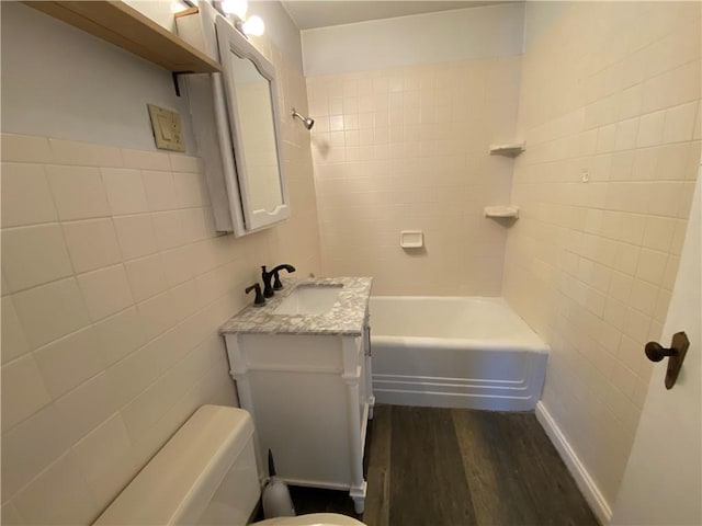 full bathroom with toilet, tile walls, tiled shower / bath combo, wood-type flooring, and vanity