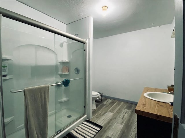 bathroom with toilet, wood finished floors, vanity, baseboards, and a stall shower