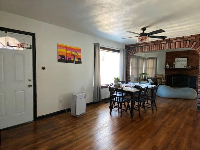 dining room featuring ceiling fan, a fireplace, baseboards, and wood finished floors