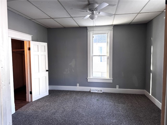 empty room featuring visible vents, dark carpet, and a drop ceiling