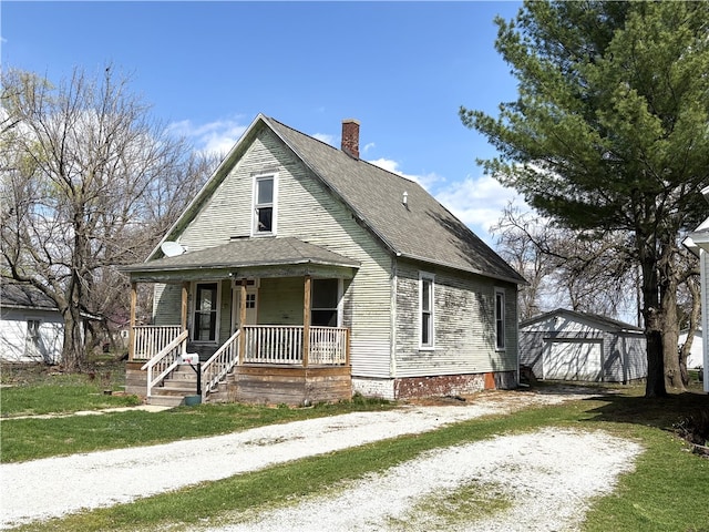 bungalow featuring a detached garage, covered porch, a chimney, an outbuilding, and driveway