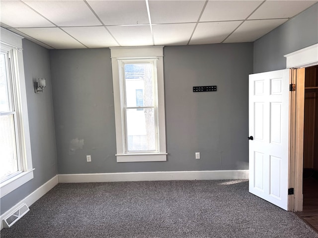 carpeted empty room featuring a paneled ceiling, visible vents, and baseboards