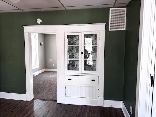 interior space featuring a drop ceiling, dark wood finished floors, visible vents, and baseboards