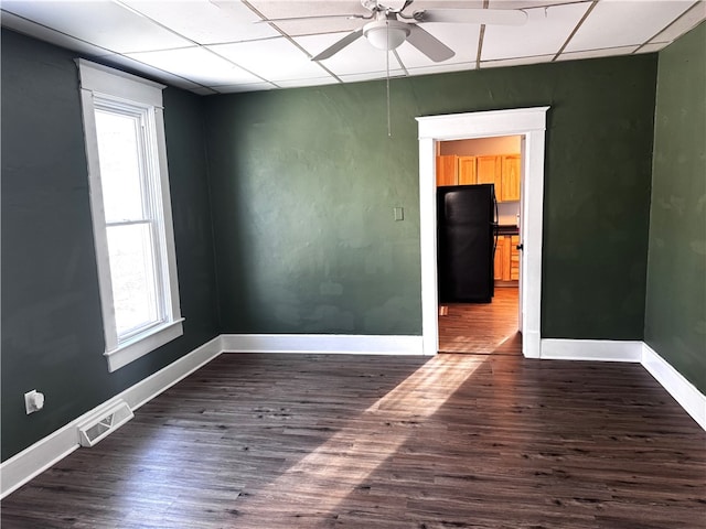 empty room with baseboards, visible vents, dark wood finished floors, a drop ceiling, and ceiling fan