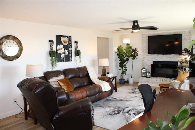 living area featuring a fireplace, wood finished floors, a ceiling fan, and baseboards