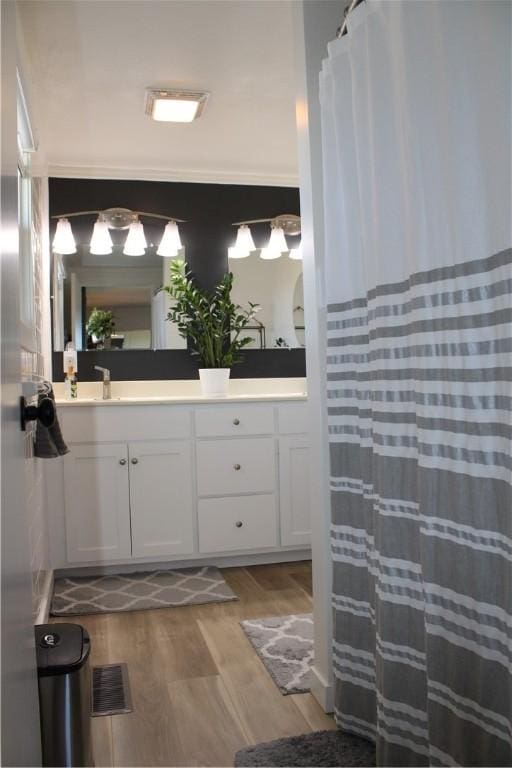 bathroom featuring a shower with curtain, wood finished floors, visible vents, double vanity, and a sink