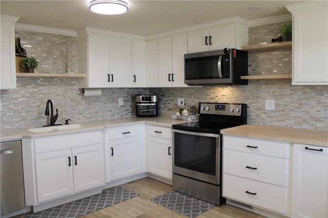 kitchen with open shelves, tasteful backsplash, appliances with stainless steel finishes, and a sink