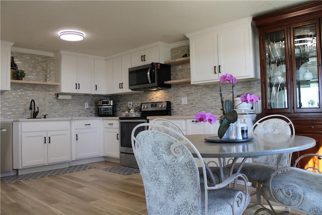 kitchen featuring open shelves, light wood-type flooring, decorative backsplash, appliances with stainless steel finishes, and a sink