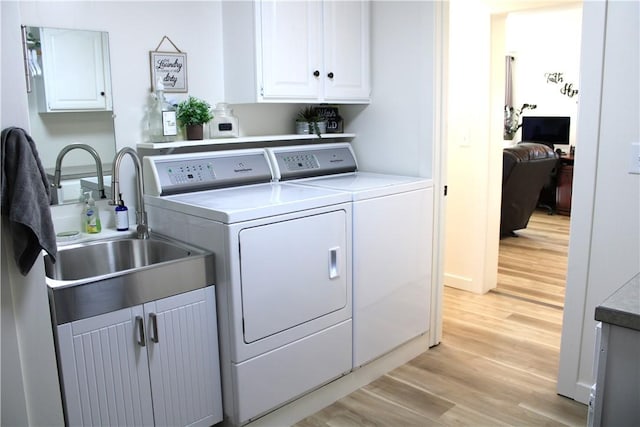 washroom with a sink, cabinet space, separate washer and dryer, and light wood finished floors