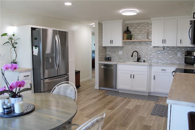 kitchen featuring backsplash, light wood-style flooring, appliances with stainless steel finishes, white cabinetry, and a sink