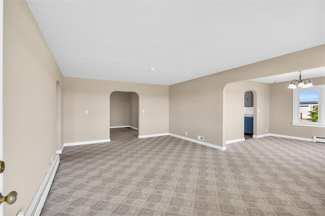 carpeted empty room featuring baseboard heating and a chandelier