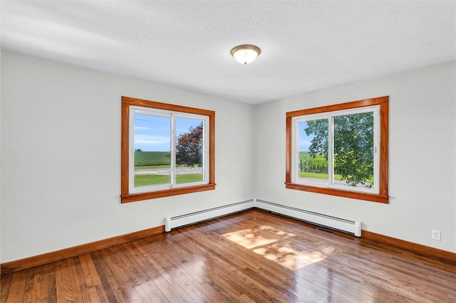 spare room with a textured ceiling, hardwood / wood-style flooring, baseboard heating, and plenty of natural light