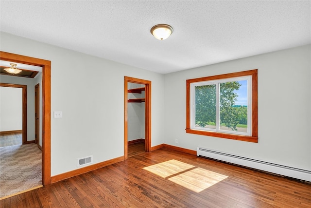 unfurnished bedroom featuring baseboard heating, hardwood / wood-style floors, and a textured ceiling