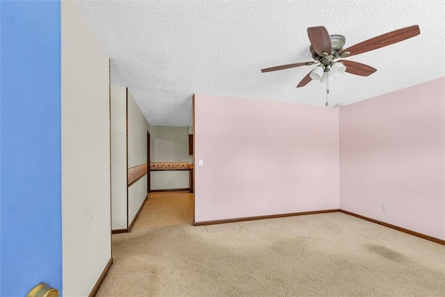 empty room with light carpet, ceiling fan, baseboards, and a textured ceiling