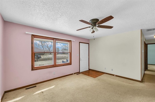 empty room featuring visible vents, light carpet, baseboards, and a textured ceiling