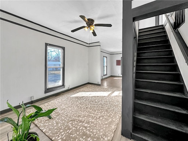 unfurnished living room with baseboards, visible vents, ceiling fan, stairway, and ornamental molding