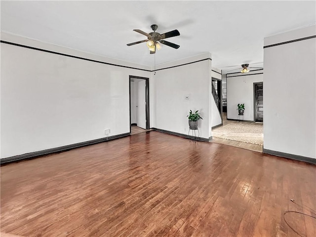 unfurnished room featuring ceiling fan, stairway, baseboards, and wood finished floors