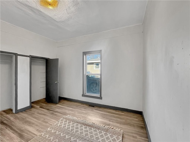 unfurnished bedroom with multiple closets, wood finished floors, visible vents, and baseboards