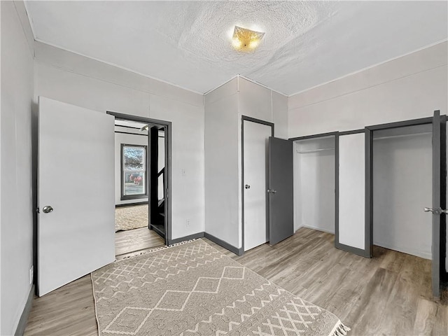 unfurnished bedroom featuring multiple closets, a textured ceiling, baseboards, and wood finished floors