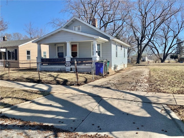 bungalow-style house with covered porch, a fenced front yard, and a chimney