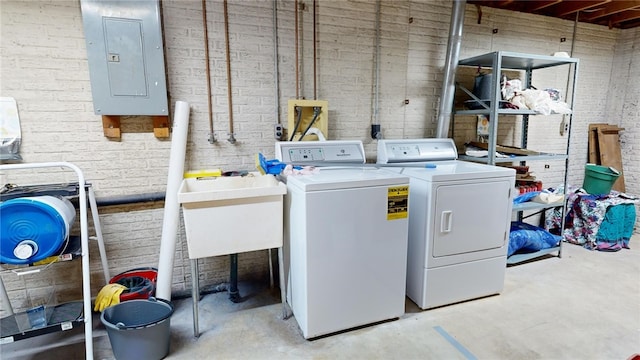 laundry area with independent washer and dryer, sink, electric panel, and brick wall