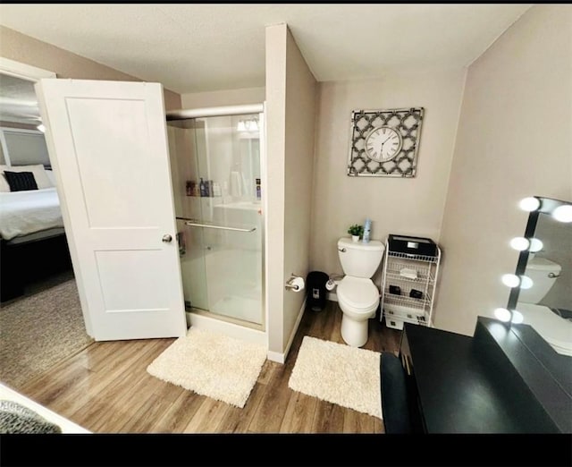 ensuite bathroom featuring toilet, ensuite bathroom, a stall shower, wood finished floors, and baseboards