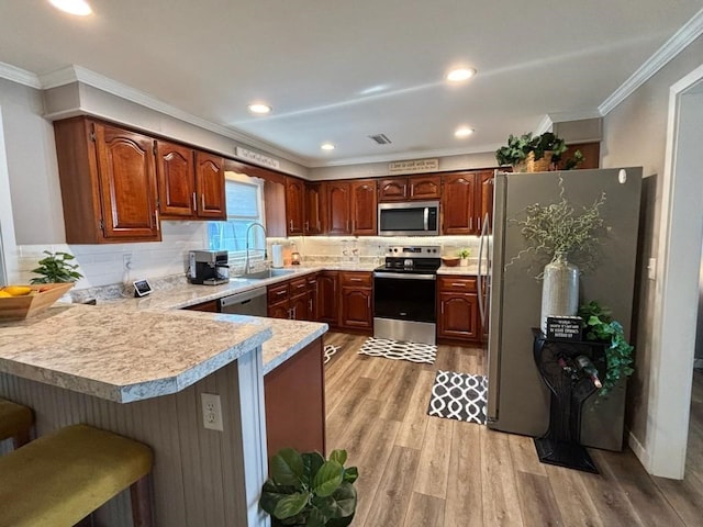 kitchen with appliances with stainless steel finishes, a peninsula, light countertops, crown molding, and a sink