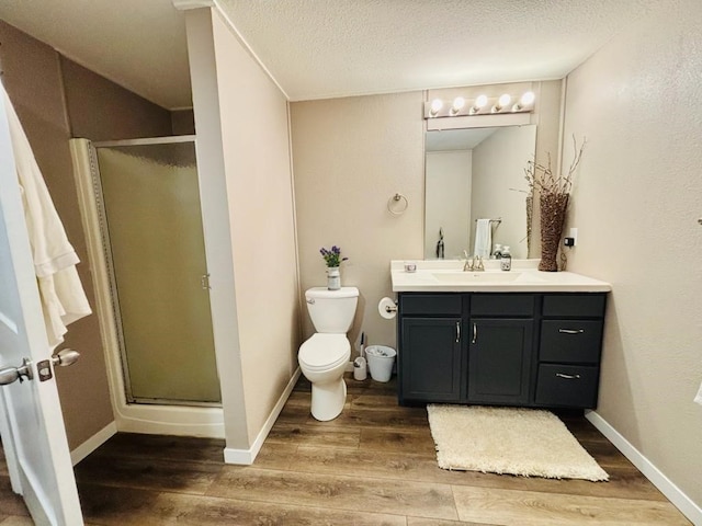 bathroom with toilet, a stall shower, a textured ceiling, vanity, and wood finished floors