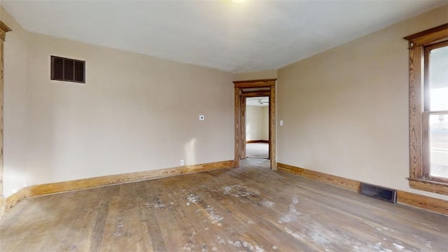 spare room featuring wood-type flooring, visible vents, and baseboards