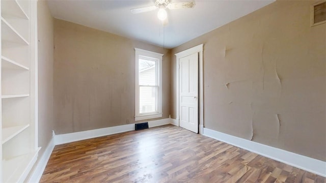 spare room with a ceiling fan, wood finished floors, visible vents, and baseboards