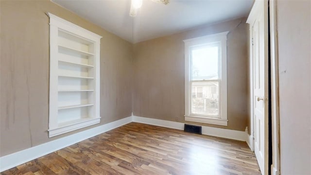 spare room featuring baseboards, built in shelves, visible vents, and light wood-style floors