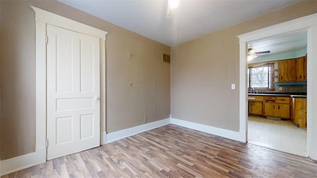 interior space with a sink, a ceiling fan, baseboards, visible vents, and light wood-style floors