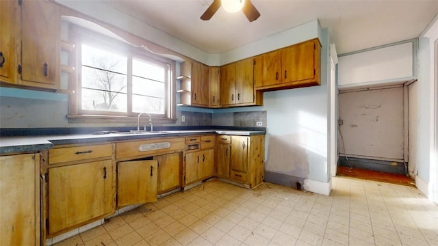 kitchen with tasteful backsplash, brown cabinetry, dark countertops, light floors, and a sink