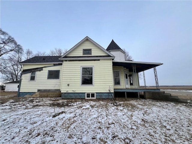 snow covered rear of property with a porch and a shingled roof