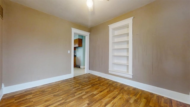 empty room with built in features, baseboards, and wood finished floors