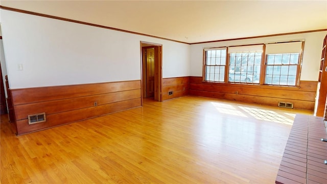 spare room with a wainscoted wall, visible vents, wood walls, and light wood-style flooring