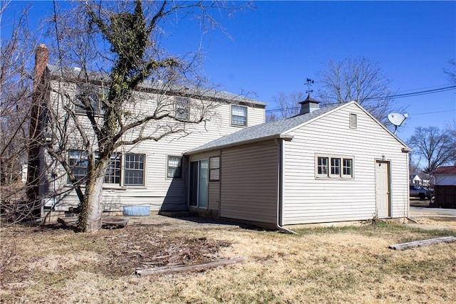 rear view of house featuring a shingled roof and a chimney