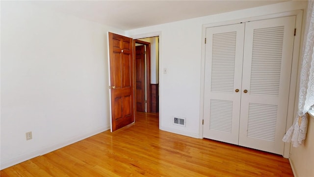 unfurnished bedroom featuring light wood-style floors, baseboards, visible vents, and a closet