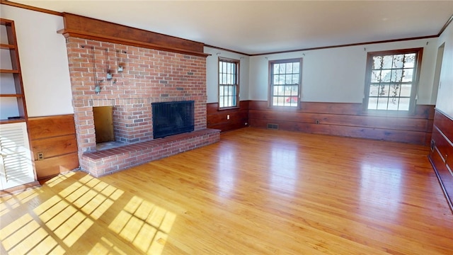 unfurnished living room featuring a brick fireplace, a wainscoted wall, visible vents, and wood finished floors