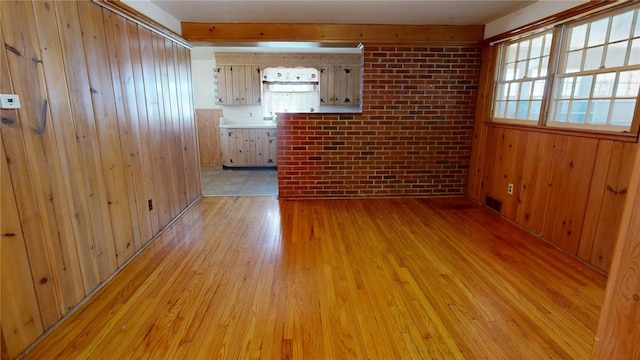 interior space with light wood-style floors, visible vents, wood walls, and brick wall