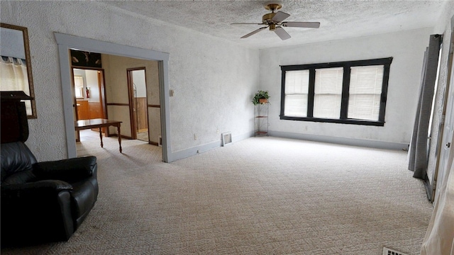 unfurnished living room with a textured wall, carpet, and ceiling fan