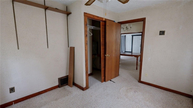 unfurnished bedroom featuring baseboards, visible vents, a textured wall, and light colored carpet