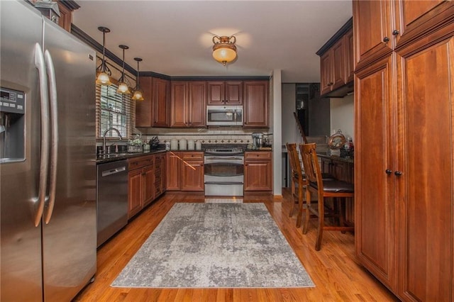 kitchen with tasteful backsplash, decorative light fixtures, light wood-style floors, stainless steel appliances, and a sink